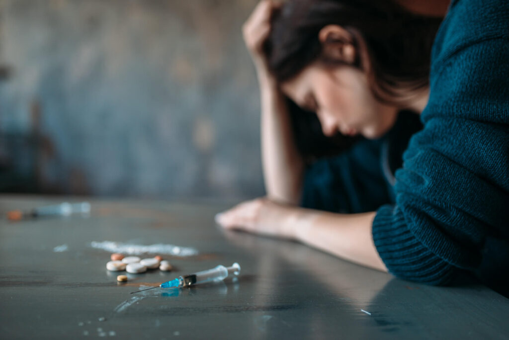 Kobieta uzależniona od narkotyków siedząca przy stole z pełnym substancji psychoaktywnych