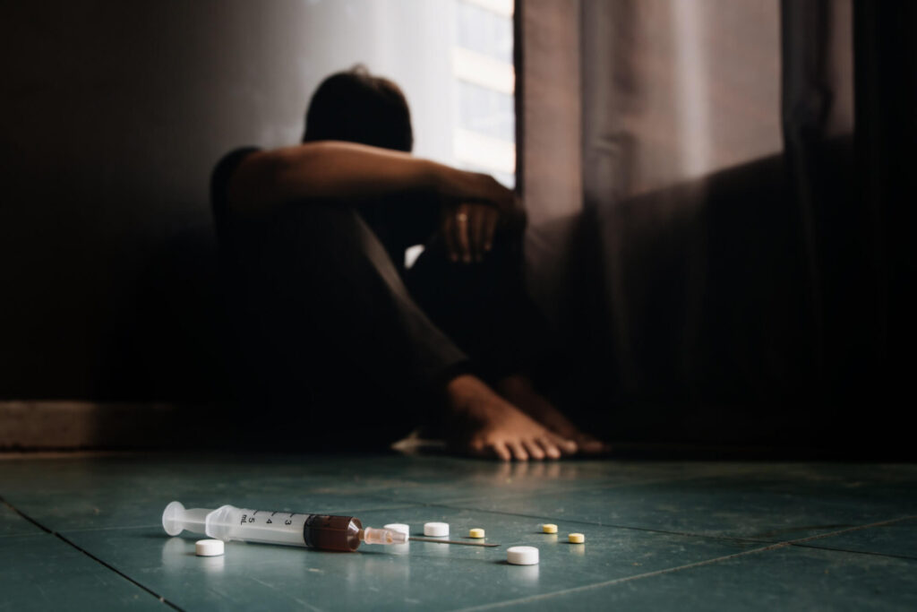 Mężczyzna siedzący załamany na podłodze obok substancji psychoaktywnych