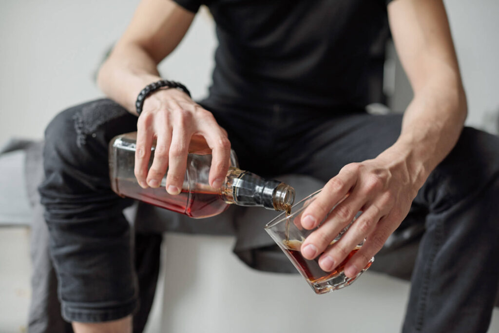 Mężczyzna nalewający alkohol do szklanki - jak przekonać osobę uzależnioną do leczenia