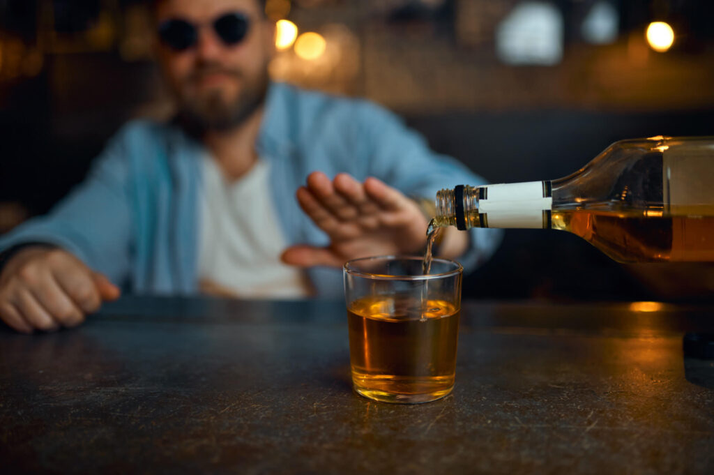 Nalewany alkohol, mężczyzna odmawiający gestem dłoni - odmowa picia
