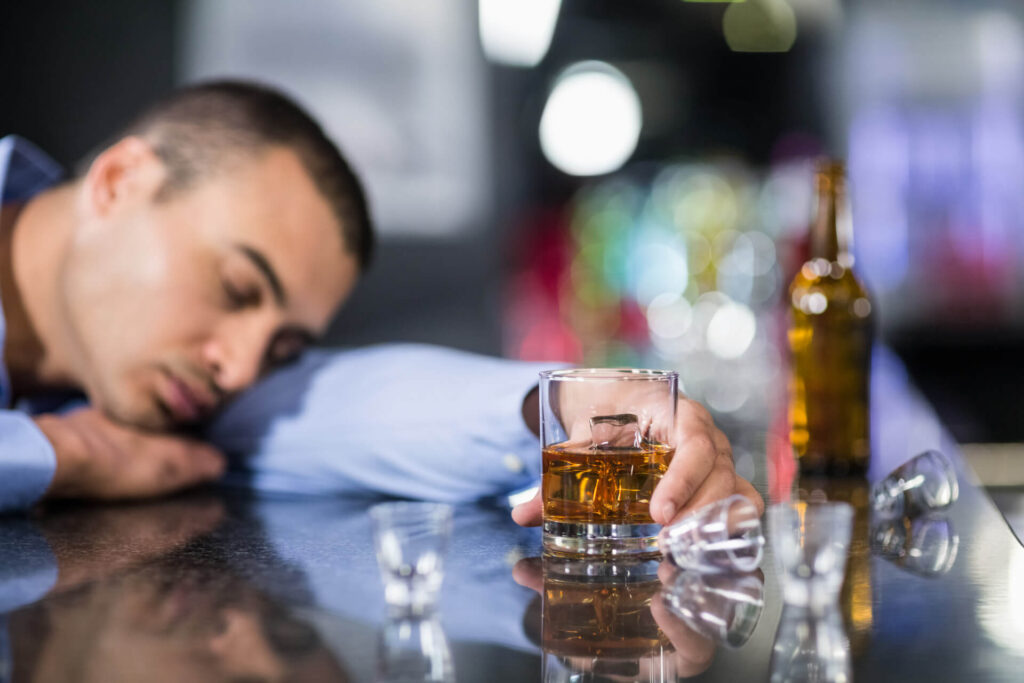 Mężczyzna nieprzytomny po alkoholu przy barze wśród kieliszków - ciąg alkoholowy