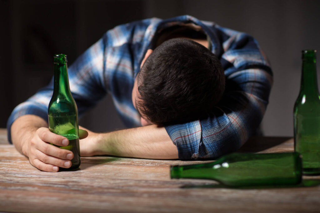 Mężczyzna leżący na barze z głową opartą o rękę, w drugiej dłoni butelka - kryzys po odstawieniu alkoholu