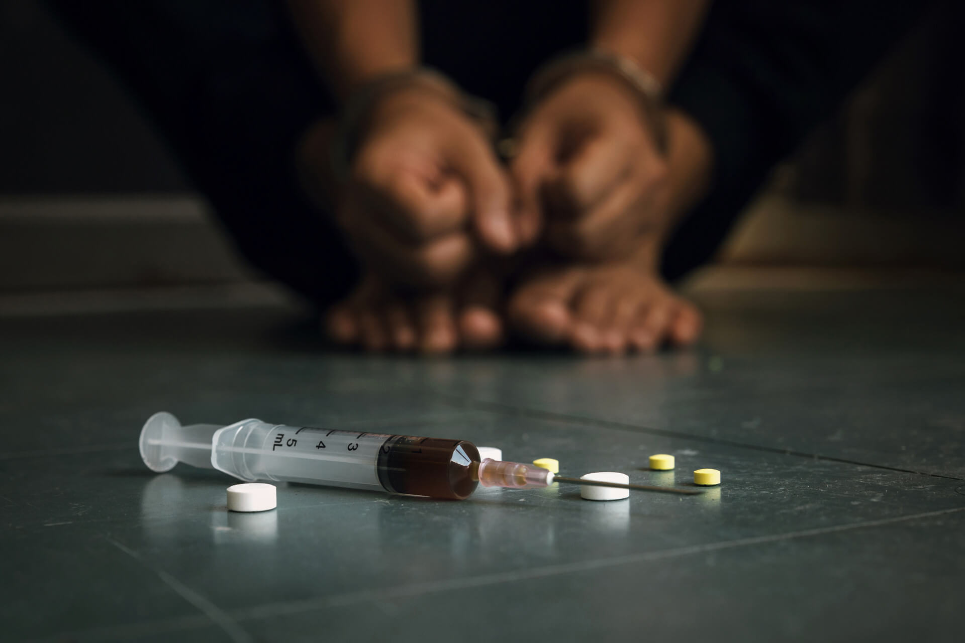 Substancje psychoaktywne leżące na podłodze, w tle zaciśnięte dłonie osoby uzależnionej od narkotyków