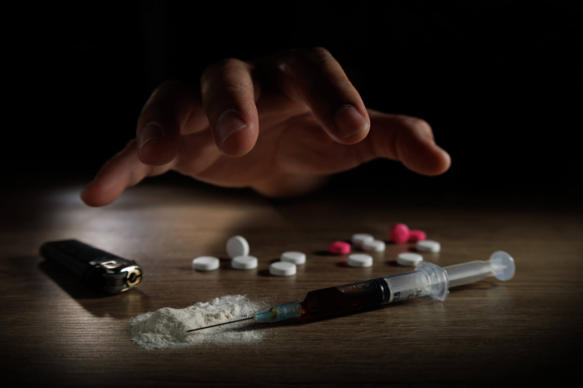 Substancje psychoaktywne leżące na stole i ręka wyciągnięta w ich stronę